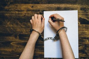 handcuffed man writing a statement